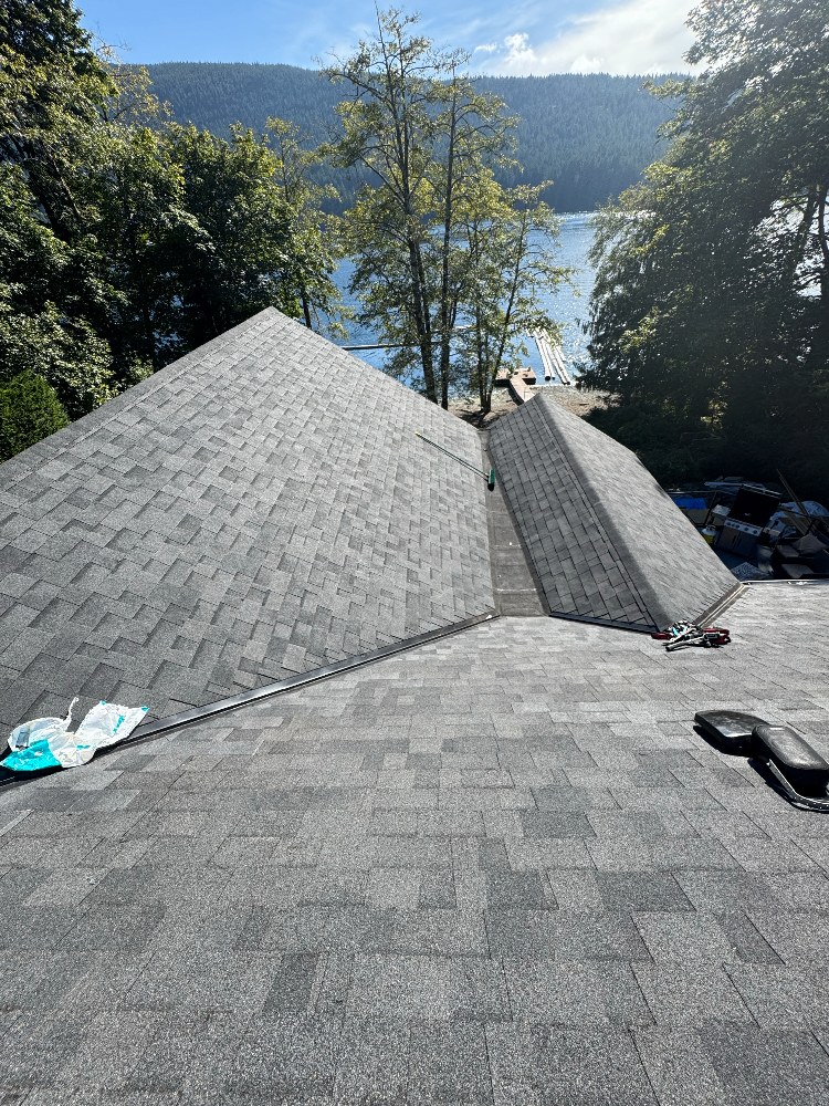 New shingle hip roof on a waterfront home with forest and inlet behind